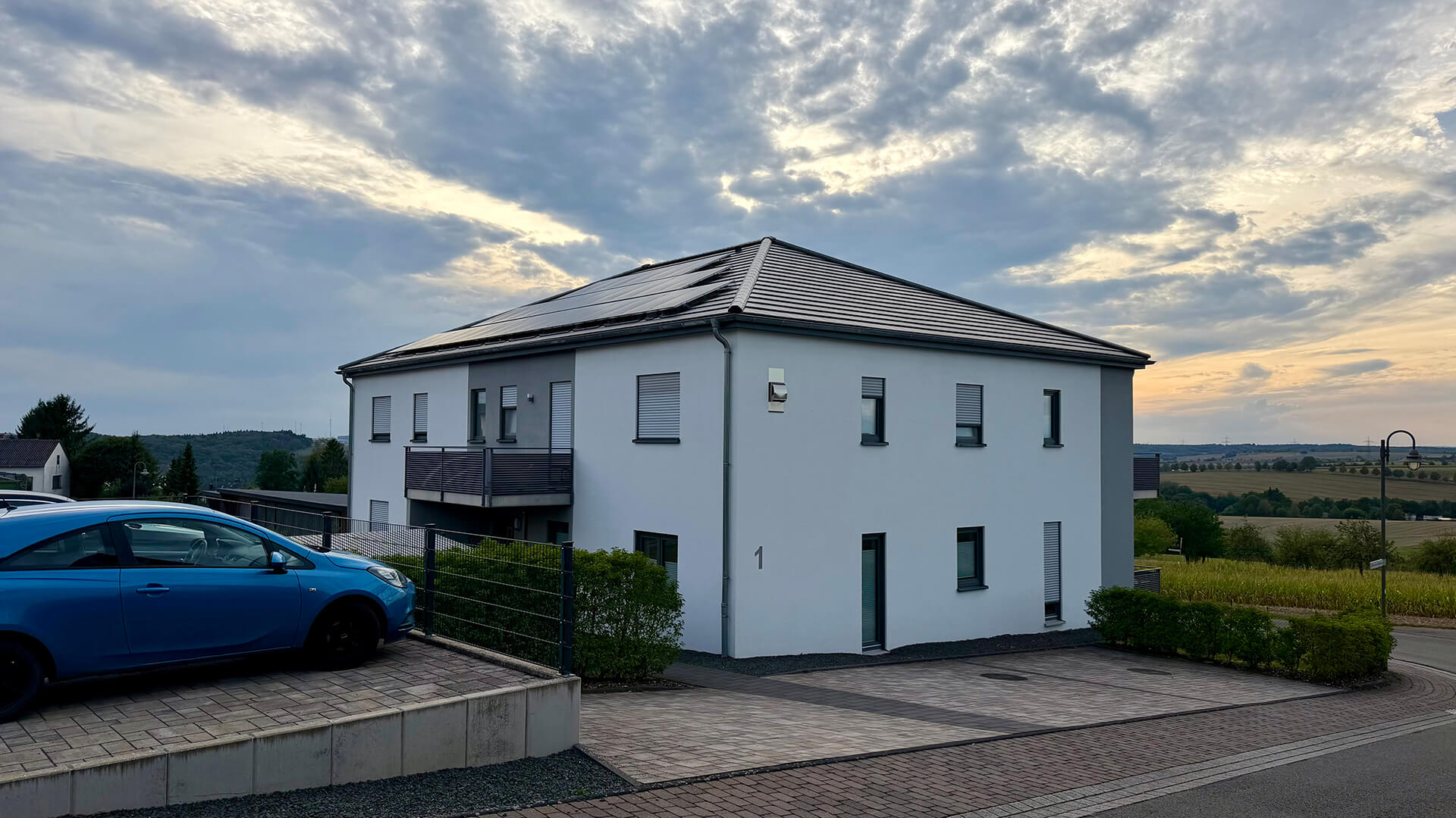 Wohngebäude im Mainzweg mit Solarmodulen auf dem Walmdach, Balkon und gepflastertem Vorplatz.